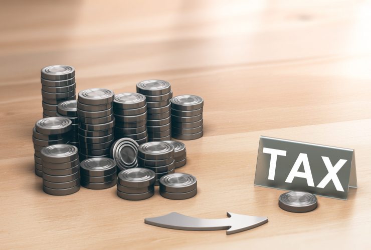 Piles of coins symbols on a wooden table and an arrow pointing a single coin with the word tax. Financial advisory and tax planning concept. 3d illustration.