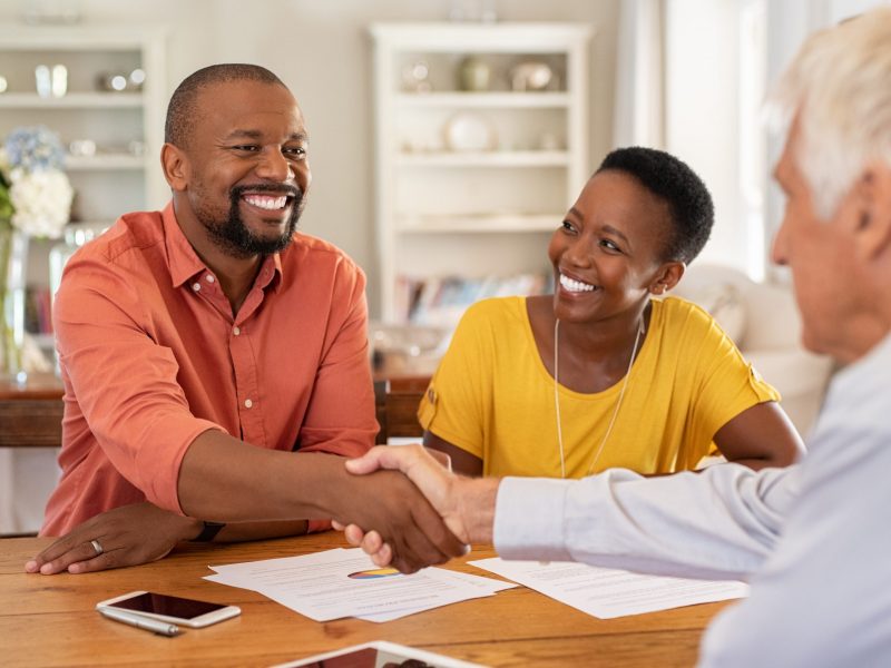 Mature black husband shaking hands with senior agent on taking loan. Happy african couple sealing with handshake a contract with financial advisor for investment. Man making sale purchase deal concluding with a handshake with estate agent.
