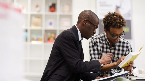 Content smart African-American business school students sitting at table and analyzing information in book while preparing financial research together